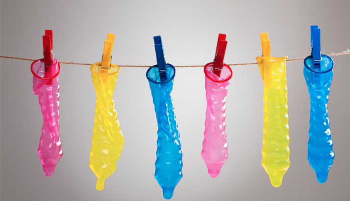 opened condoms of various colours handing from a clothes line